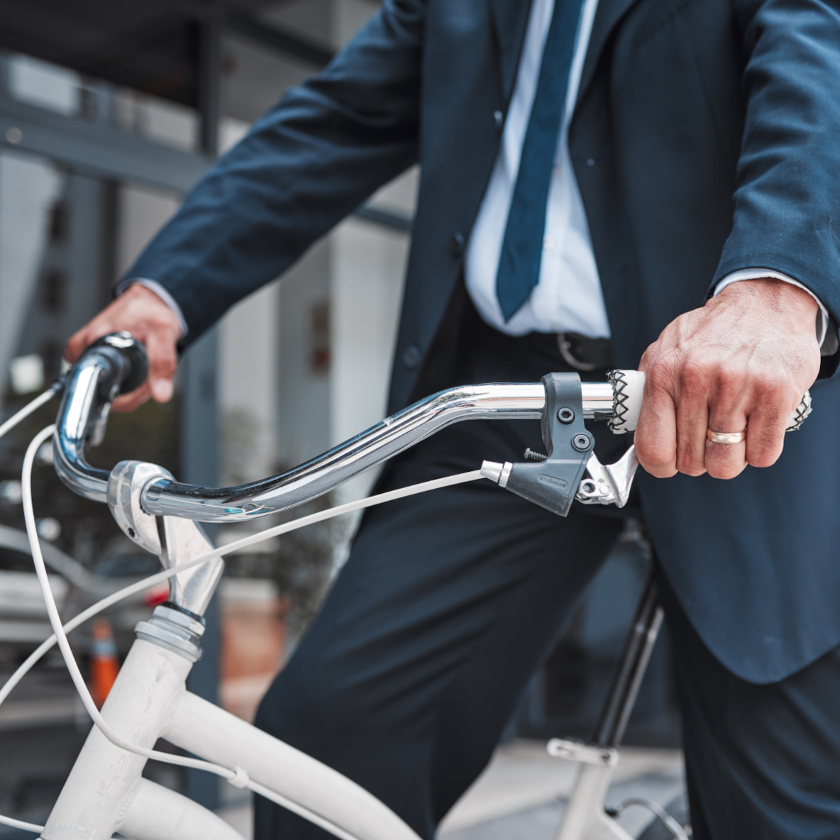 Man sieht einen Geschäftsmann, der ein Fahrrad fährt, im Hintergrund verschwommene Häuserfassaden.