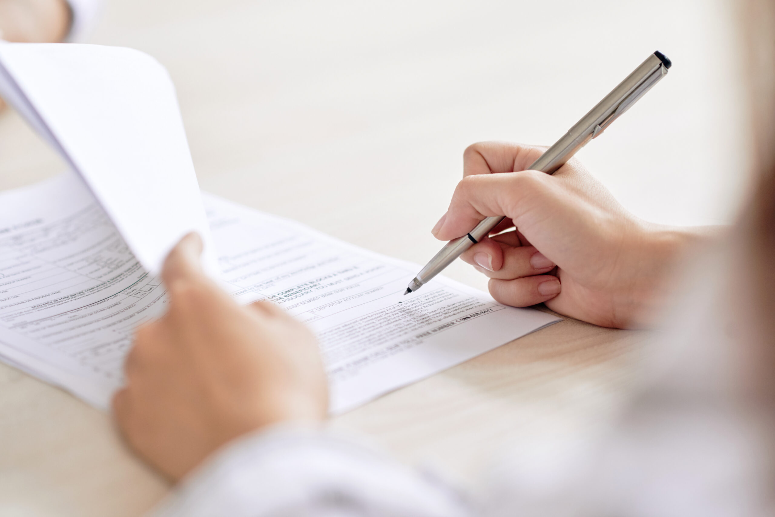 Person mit Stift, die einen Vertrag am Schreibtisch unterzeichnet